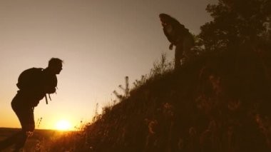 Bir kadın gezgin gün batımı ışığında bir tepeye tırmanan bir adama uzanır. gezginler el ele tutuşarak uçuruma tırmanıyorlar. iş adamlarının takım çalışması. Mutlu bir aile tatilde. Yavaş çekim.