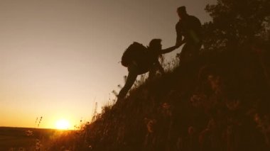 erkek gezgin tepeye tırmanan bir kadın yolcu elini uzatır. Turistler gün batımında el ele tutuşarak dağa tırmanıyorlar. iş adamlarının takım çalışması. Mutlu bir aile tatilde. Yavaş çekim
