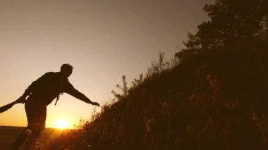 Turistler gün batımında el ele tutuşarak dağa tırmanıyorlar. erkek gezgin bir tepeye tırmanma bir kadın gezgin elini uzatır. iş adamlarının takım çalışması. Mutlu bir aile tatilde. Yavaş çekim