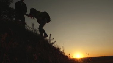 turistler gün batımında el ele tutuşarak goy aşağı inerler. erkek gezgin, tepenin tepesinden inen bir kadın yolcunun elini tutar. iş adamlarının takım çalışması. Mutlu aile tatilde.