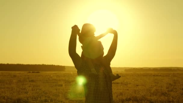 Papa trägt sein geliebtes Baby auf den Schultern, das bei Sonnenuntergang über das Feld läuft. Ein Kind mit Eltern geht abends bei Sonnenuntergang spazieren. Kleine Tochter reitet mit Papa auf den Schultern im Park. Zeitlupe. — Stockvideo