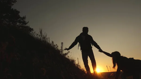 tourists go down from the goy in the sunset, holding hands. male traveler holds the hand of a female traveler going down from top of the hill. teamwork of business people. Happy family on vacation.