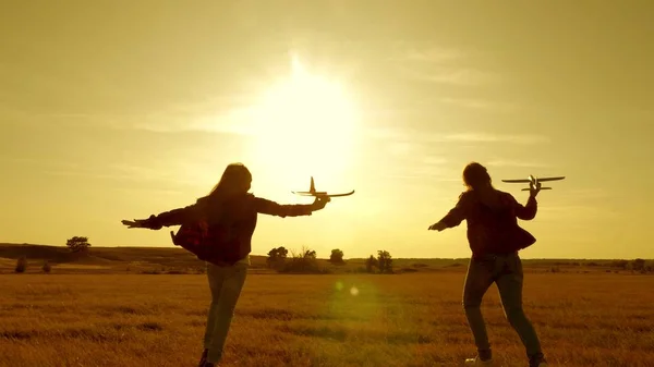 Drömmar om att flyga. Glad barndomsidé. Två flickor leker med ett leksaksplan vid solnedgången. Barn på bakgrunden av solen med ett flygplan i handen. Silhuett av barn som leker på planet — Stockfoto