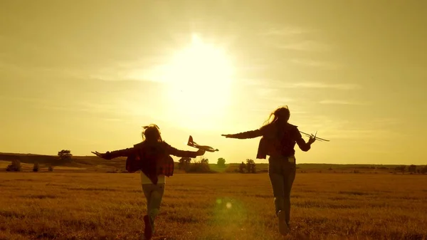 Sogni di volare. Concetto infanzia felice. Due ragazze giocano con un aereo giocattolo al tramonto. Bambini sullo sfondo del sole con un aereo in mano. Silhouette di bambini che giocano sull'aereo — Foto Stock