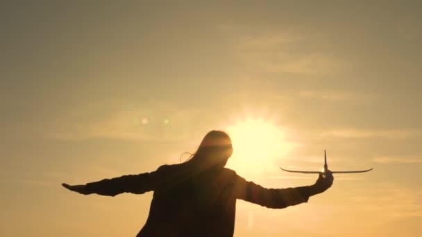 Chica feliz corre con un avión de juguete en un campo en la luz del atardecer. niños juegan juguete avión. adolescente sueña con volar y convertirse en piloto. la chica quiere convertirse en piloto y astronauta. Movimiento lento — Vídeo de stock