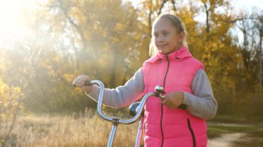 çocuk parkta bir bisiklet ile seyahat. genç kız yürüyor. Genç bir kız yolda yürür ve bisiklete biner. Genç bisiklet ile sonbahar yürümek. spor yaşam tarzı. Yavaş çekim