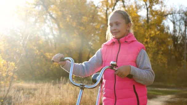 Kind reist met een fiets in het Park. jong meisje loopt. Een jong meisje loopt langs de weg en rijdt op een fiets. Tiener lopen herfst met fiets. sport lifestyle. Slow Motion — Stockvideo