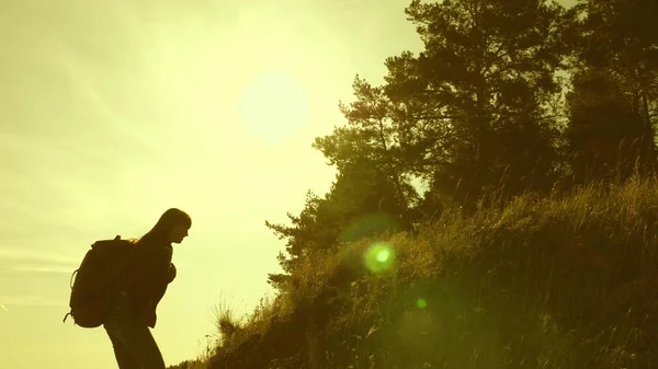 Le ragazze viaggiatrici scalano la montagna, si offrono una mano a vicenda, aiutando a scalare la collina. Famiglia di turisti che viaggiano al tramonto. sorelle con zaini viaggiano scalando la montagna al sole. lavoro di squadra turistico — Foto Stock