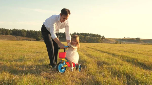 Gelukkige vader leert kleine dochter fietsen. Papa speelt met een klein kind op het gazon. Een kind leert fietsen. ouders en dochtertje lopen in het park. concept van gelukkig gezin en jeugd. — Stockfoto