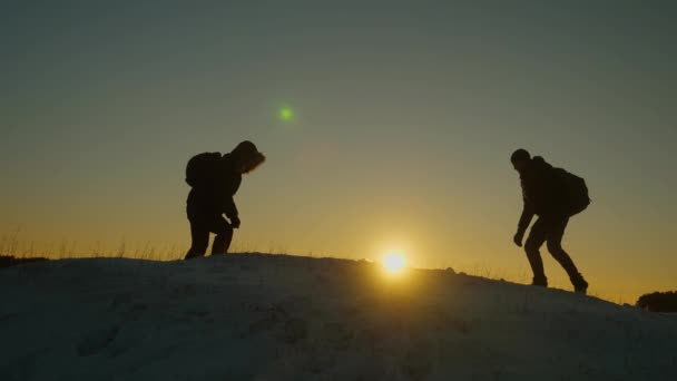 Gli arrampicatori si incontrano sulla cima di una montagna innevata e si godono il loro successo, alzano le mani e saltano gioiosamente. I turisti di uomini con zaini hanno raggiunto la cima di collina in inverno un tramonto. concetto di turismo sportivo — Video Stock