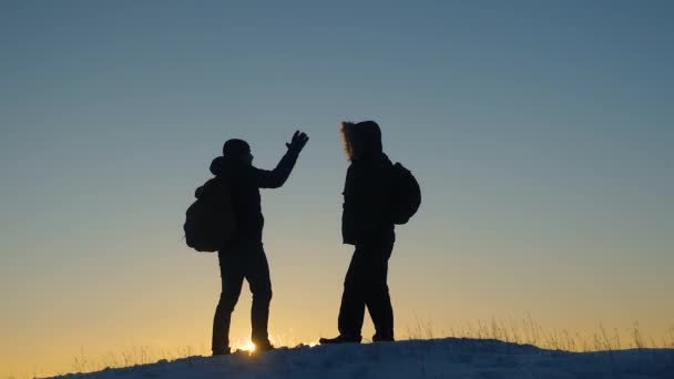 Climbers meet on top of snowy mountain and enjoy their success, raise their hands and jump joyfully. Men tourists with backpacks reached top of hill in winter a sunset. sports tourism concept — Stock Video