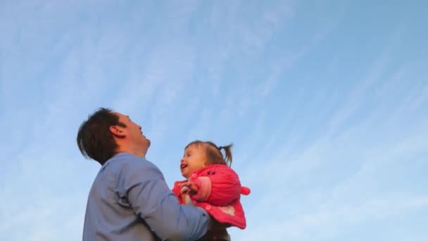 Otec hodil šťastné dítě na modrou oblohu. Táta si hraje se svou dcerou v parku. koncepce šťastné rodiny. Táta vyhazuje dítě vysoko proti obloze. — Stock video