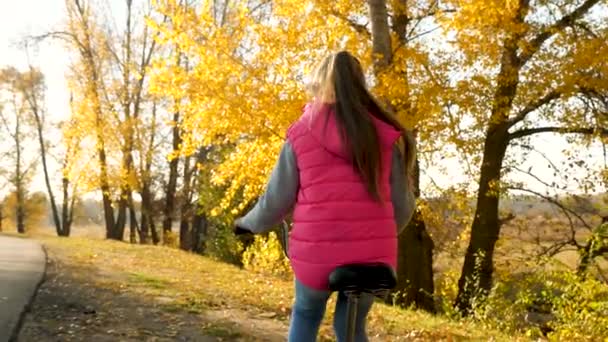 Chica viaja en bicicleta en el camino. deportista adolescente paseo en bicicleta. Una joven con una chaqueta verde monta una bicicleta en el camino al parque de otoño . — Vídeo de stock