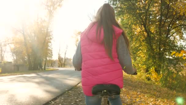 Menina viaja de bicicleta no caminho. passeio esportivo adolescente em uma bicicleta. Uma jovem de jaqueta verde monta uma bicicleta na estrada para o parque de outono . — Vídeo de Stock