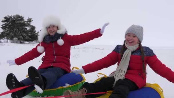 Niños felices en trineo en la nieve en el invierno y agitando sus manos. familia juega en el parque de invierno durante las vacaciones de Navidad. niños se ríen y se regocijan. En cámara lenta. concepto de una familia feliz . — Vídeo de stock