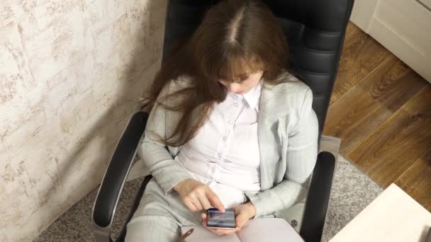 Güzel bir iş kadını telefonda konuşuyor, sandalyede çıplak ayakla oturuyor, dinleniyor ve çay içiyor, kahve içiyor. Ofisteki mutlu kız elinde bir fincan kahveyle akıllı telefonla konuşuyor.. — Stok video