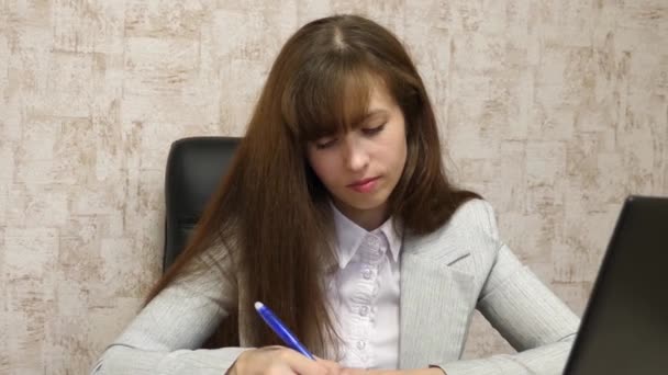Affärskvinna sitter i stol på kontoret vid datorn och antecknar i anteckningsboken. ung kvinnlig entreprenör som arbetar bakom laptopen. sekreterare skriver penna i en anteckningsbok — Stockvideo