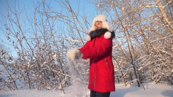 Chica feliz vomita nieve con sus manos al atardecer en el bosque. Nieve cae y brilla al sol. niño juega en invierno en el parque para las vacaciones de Navidad . — Vídeo de stock