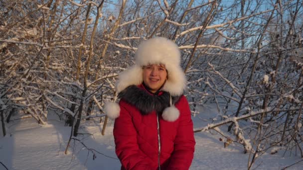 幸せな女の子は森の日没時に手で雪を投げる。雪が降り、太陽の下で輝きます。子供はクリスマス休暇のために公園で冬に遊ぶ. — ストック動画