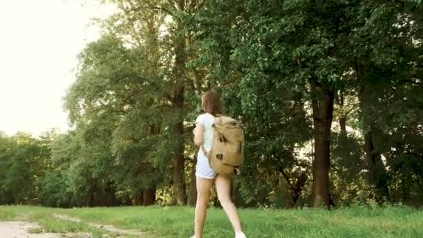 背着背包的那个女孩沿着森林路散步。徒步旅行的女人走在森林里。快乐的徒步旅行女孩在夏天的公园。青少年 女孩 冒险 在 度假. — 图库视频影像