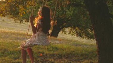 Çocuk parkta güneşin altında salıncakta sallanıyor. İp üzerinde sallanan genç bir kız meşe dalında sallanıyor. Genç kız yaz akşamı ormanda salıncakta sallanmaktan hoşlanıyor. Mutlu aile ve çocukluk kavramı.