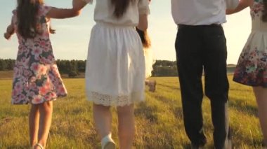 Anne, baba ve kız kardeşleriyle birlikte güneşte yürüyen küçük bir kız. Mutlu, genç bir aile. Çocuklar, anne ve babalar gün ışığında çayırlarda oynuyorlar. Mutlu aile kavramı.