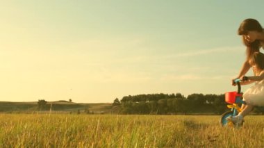 Çocuk bisiklet sürmeyi öğreniyor. Ebeveynler ve küçük kızları parkta yürürler. Mutlu anne küçük kızına bisiklet sürmeyi öğretiyor. Annem çimenlikte küçük çocukla oynuyor. Mutlu aile ve çocukluk kavramı.