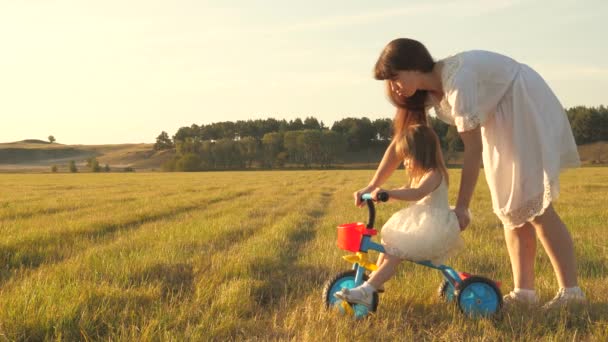 Moeder leert dochter om een fiets te rijden. Moeder speelt met haar kleine dochter. een klein kind leert fietsen. concept van Happy Childhood. — Stockvideo