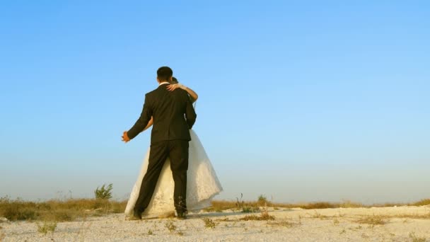 Junge und Mädchen tanzen im Sand und lächeln sich an. romantisches Paar Mann und Frau amüsieren sich gemeinsam vor blauem Himmel — Stockvideo