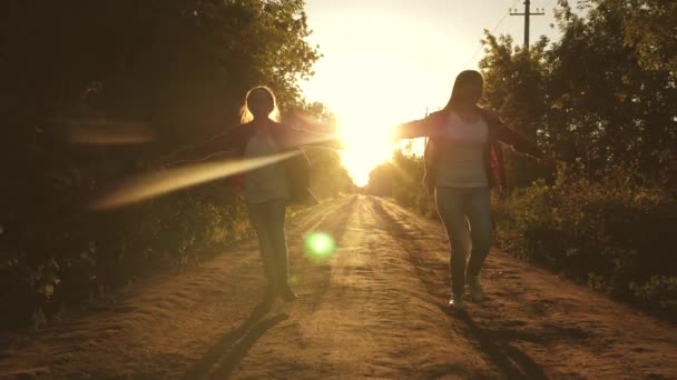 Caminhante. crianças viajantes. meninas adolescentes viajar e dar as mãos. meninas felizes viajantes com mochilas correr ao longo estrada país de mãos dadas em raios do sol brilhante. conceito de turismo desportivo e — Vídeo de Stock