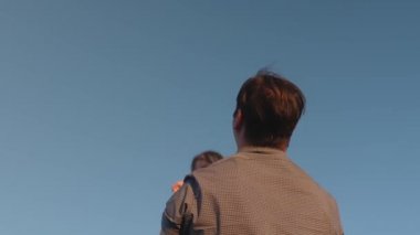 Babam küçük bir çocukla oynuyor. Babam mavi gökyüzüne kızını kustu. Mutlu aile akşamları gökyüzüne karşı oynuyor. Babası bebeği kusuyor, çocuk gülümsüyor. Ağır çekim. Mutlu aile