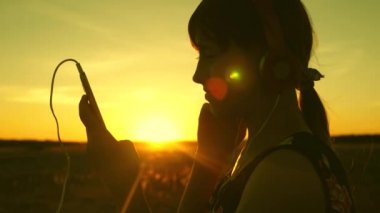 Kız gezer ve sıcak güneşin altında müzik dinler. Genç kız müzik dinliyor ve gün batımını seyrediyor. Parkta güneşin doğuşunda kulaklıkla dans eden mutlu kız..