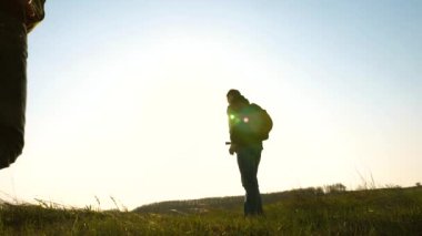 Sırt çantalı gezginler birbiri ardına gidiyor. Zafer ve başarı için takım çalışması. Sırt çantalı turistler parlak güneş ışınlarıyla tarlada yürüyorlar. İş adamlarının işbirliği. Yavaş çekim