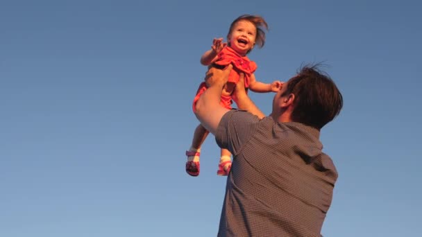 Отец бросает своего ребенка в голубое небо Папа играет с маленькой дочерью, ребенок улыбается и радуется. Медленное движение. Счастливая семья играет вечером на фоне неба . — стоковое видео