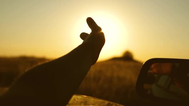 Meninas mão acena o sol. Viajar de carro. mão motoristas está brincando com o sol da janela do carro contra o pôr do sol bonito . — Vídeo de Stock