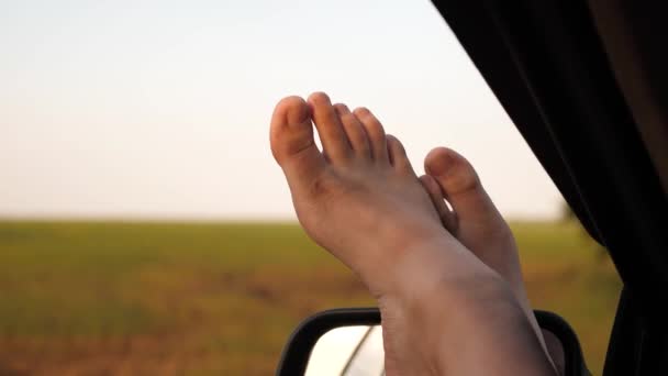 Blote voeten van een meisje in een autoruit, schittering van de zon, rijden op een auto op een landweg. vrouw reist met de auto. jonge vrouw houdt van reizen in een auto, het zetten van haar benen uit een open raam. — Stockvideo