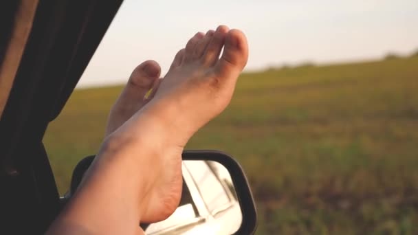 Pieds nus d'une fille dans une fenêtre de voiture, éblouissement du soleil, chevauchant une voiture sur une route de campagne. femme voyage en voiture. jeune femme aime voyager dans une voiture, mettant ses jambes par une fenêtre ouverte . — Video