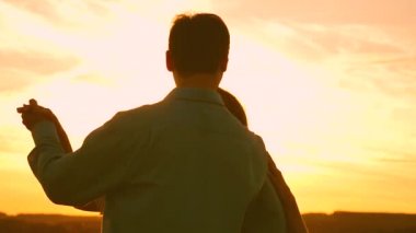 Genç çift sahilde gün batımında dans ediyor. Sevgi dolu erkek ve kadın gölün arka planda güneşin parlak ışınları dans. Yaz parkında akşam mutlu adam ve kız vals.