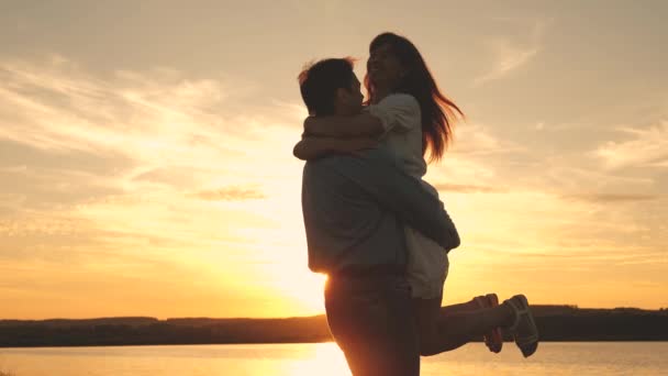Młoda para kręci się i tańczy o zachodzie słońca na plaży. Kochający mężczyzna i kobieta tańczą na tle jeziora. — Wideo stockowe