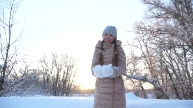 Noel tatili için çocuk parkta oynuyor. Kar yağıyor. Çocuk Noel tatili için parkta oynuyor. Mutlu kız gün batımında kar taneleri fırlatıyor ve kış parkında gülümsüyor. Yavaş