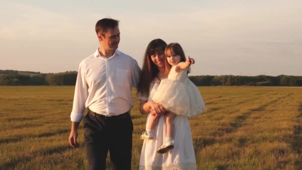 Padre e hija pequeña, madre, caminando en un campo bajo el sol. niño, papá y mamá juegan en el prado bajo el sol. concepto de una infancia feliz. Feliz familia joven. concepto de una familia feliz . — Vídeos de Stock