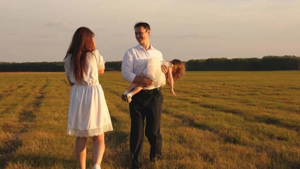 Concept van een gelukkige jeugd. kind, vader en moeder spelen in de weide in de zon. Moeder, vader en dochtertje wandelen in een veld in de zon. Gelukkige jonge familie. concept van een gelukkig gezin. — Stockfoto