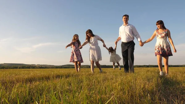 Barn, pappa och mamma leker på ängen i solskenet. mor, far och dotter med systrar som går i fält i solen. Lycklig ung familj. begreppet lycklig familj. — Stockfoto