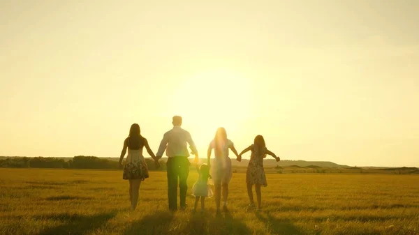 Madre, padre e hija pequeña con hermanas caminando en el campo bajo el sol. Feliz familia joven. Los niños, papá y mamá juegan en el prado bajo el sol. El concepto de una familia feliz . —  Fotos de Stock