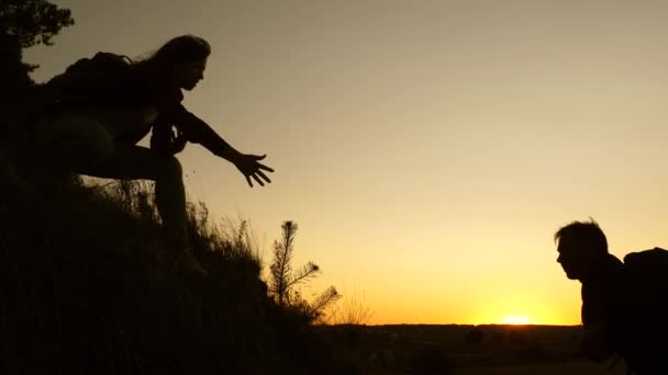Voyageur femelle tient la main d'un voyageur masculin aidant à grimper au sommet de la colline. Les touristes escaladent la montagne au coucher du soleil, en se tenant la main. travail d'équipe des partenaires commerciaux. Bonne famille en vacances . — Video