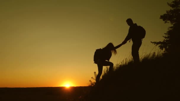 Viajante do sexo masculino segura a mão de uma viajante do sexo feminino ajudando a subir o topo da colina. Os turistas escalam a montanha ao pôr do sol, de mãos dadas. trabalho em equipe de parceiros de negócios. Família feliz em férias . — Vídeo de Stock