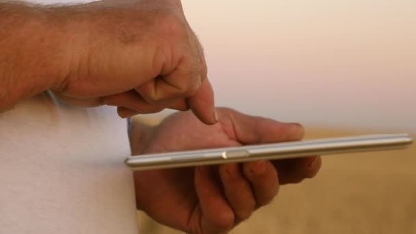 Mãos de um agricultor com um tablet. close-up. homem de negócios com um tablet avalia uma colheita de grãos. Agricultor com um tablet funciona em um campo de trigo. Colheita de cereais. homem de negócios verifica a qualidade dos grãos . — Vídeo de Stock