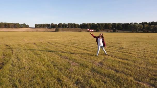 Uma adolescente com cabelos longos brinca em um campo com um avião e ele voa para a frente. A criança sonha em se tornar um piloto. Uma menina feliz quer se tornar um piloto e um astronauta — Vídeo de Stock