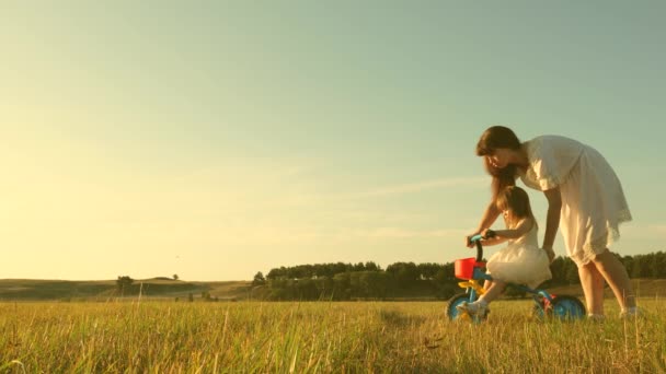 Η μαμά διδάσκει στην κόρη να κάνει ποδήλατο. Η μητέρα παίζει με την κορούλα της. ένα μικρό παιδί μαθαίνει να κάνει ποδήλατο. έννοια της ευτυχης παιδικής ηλικίας. — Αρχείο Βίντεο