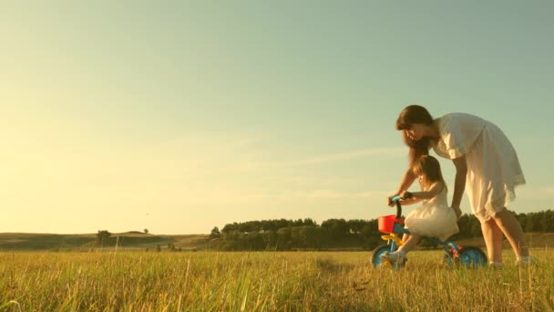 A mãe ensina a filha a andar de bicicleta. A mãe brinca com a filha. uma criança pequena aprende a andar de bicicleta. conceito de infância feliz . — Vídeo de Stock